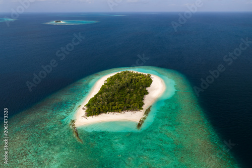 Foto Aerial view of a tiny uninhabited island in the Maldives, white sand crescent, shallow turquoise reefs, Indian Ocean, midday light, calm seas, distant atolls