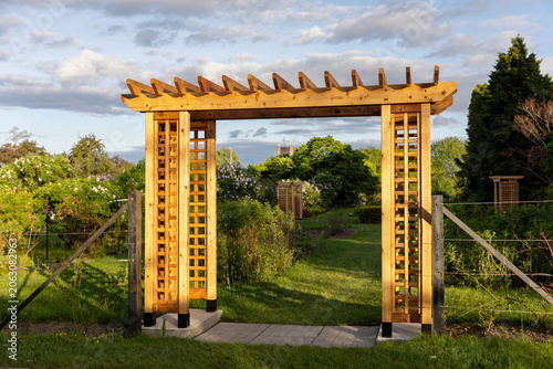 Wooden garden arbor in public park landscape. Timber pergola structure over path in blooming spring Ornamental Gardens in Ottawa, Canada.