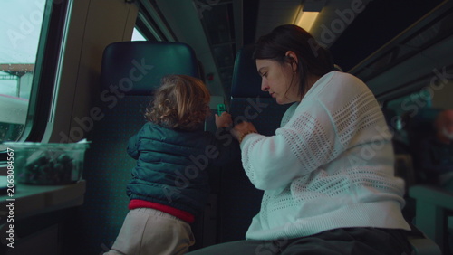 Valokuva Toddler standing on train seat facing backrest playing with toy as mother watche