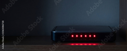 Wi-fi router with red warning lights on wooden shelf. Internet access restriction and connection error concept. Digital security blackout and social media blocking network failure.