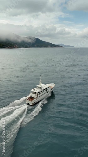 Aerial Drone Tracking Shot White Luxury Yacht Speeding on Ocean with Mountain and Cloudy Sky Background
