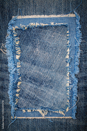 Denim fabric patch placed on blue jean background showing texture and wear in a textile setting