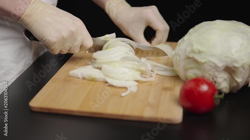 Gloved hands slicing onion on a wooden board