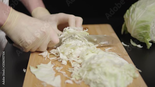 Gloved hands slicing cabbage on a wooden board