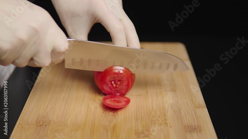 Gloved hands slicing a tomato on a wooden cutting board