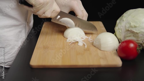 Gloved hands slicing onion on a wooden board