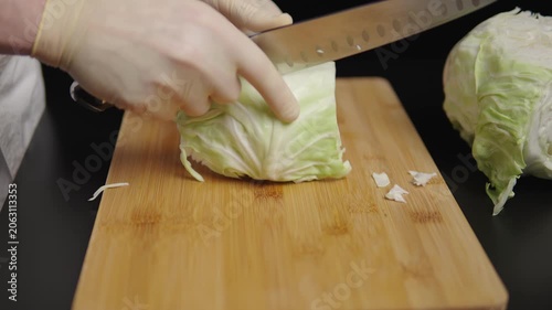 Hands shredding cabbage on a wooden cutting board