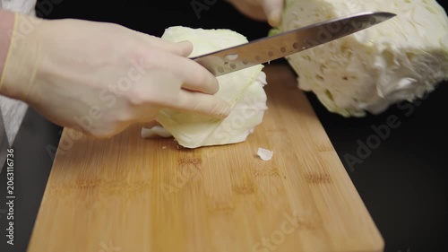 Hands slicing cabbage on a wooden board