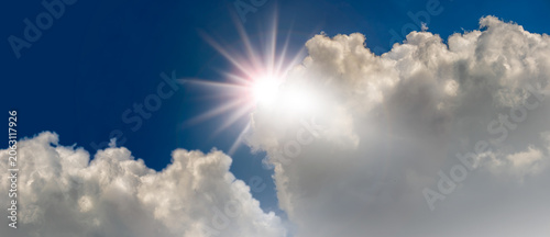 Картината върху платно Bright sun rays emerging from cumulus clouds in blue sky, Bright sunlight shining through towering white clouds against a deep blue sky
