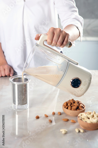 Foto Person pouring fresh almond milk from a cream-colored blender into a glass strainer
