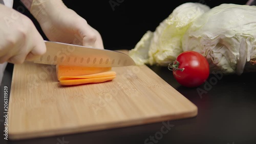 Hand slicing carrot on wooden board in kitchen