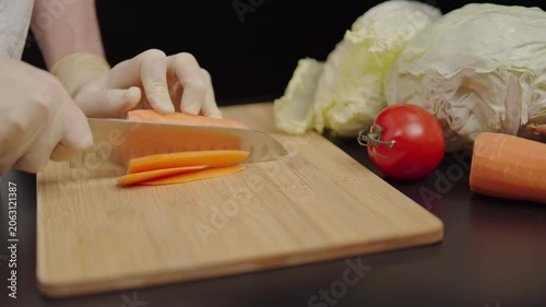 Hands slicing carrot on a wooden cutting board