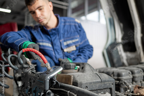 A professional mechanic in a blue work uniform is seen inspecting the intricate components of a truck engine under the hood. His expertise assures vehicle efficiency and dependable performance.