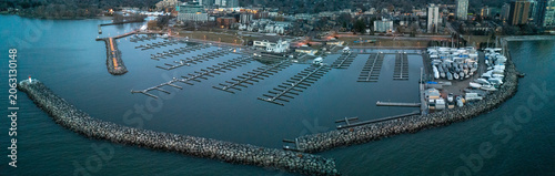 A stunning, wide panoramic drone photograph capturing the sweeping stone breakwater wall, rows of empty winter boat slips, and dry-docked yachts at Bronte Harbour on Lake Ontario at early dawn.