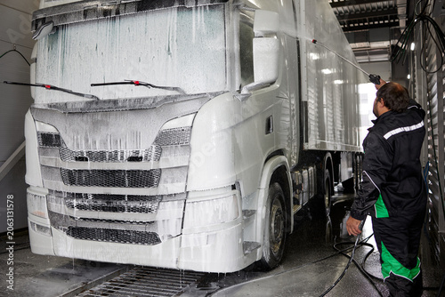 A skilled professional meticulously washes a pristine white truck cab using foam in a large car wash hangar, showcasing the effectiveness of modern cleaning techniques in a vibrant setting.