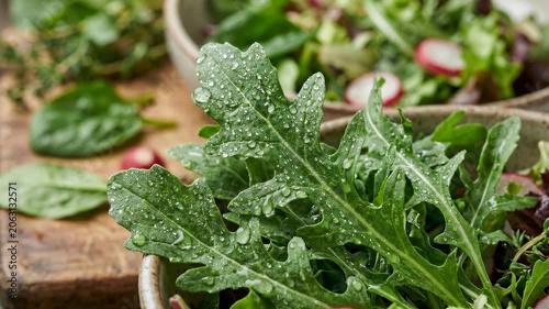 Slow motion tracking close up of salad leaves with water droplets glistening in ceramic bowl on wooden table in kitchen during morning prep fresh healthy mood