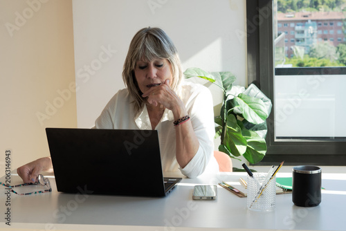 Bild auf Leinwand Mature woman working on laptop at bright desk