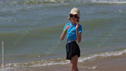 Pretty little girl in a swimsuit, sun glasses and hat relaxing on the beach near sea. Smiling cute little girl on vacation. Adorable girl in a big straw hat looks at the sea. Summer travel concept