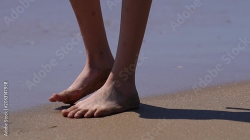 Teenage girl's legs on the beach, small gentle waves covering the child's legs, the child playing with the waves