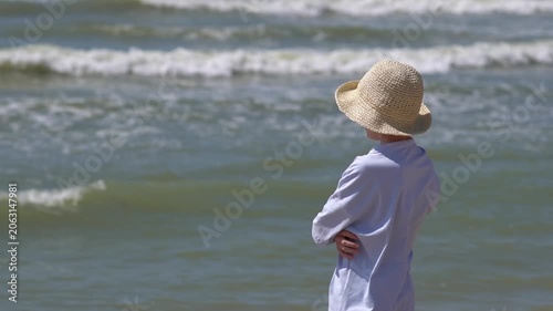A teenager wearing a hat stands on a tropical island beach, admiring the sunset. A peaceful summer getaway or vacation; summer travel concept.