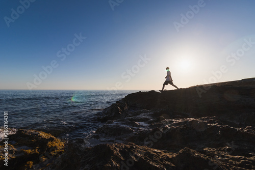 Silhouette of an 11 year old boy walking on rocky coast in Kato Gouves against the bright sun over the sea