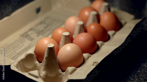 Brown eggs sit in a cardboard carton. Soft lighting pases from side to side creating long shadows.