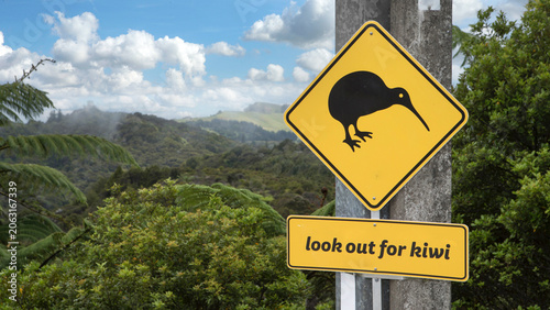 Roadsign warning to look out for crossing Kiwi's near Tauranga Bay New Zealand. Mountains and forest in background.