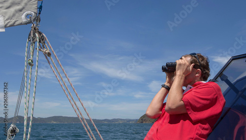 Man at sailing boat at sea with binoculars. Bay of Islands near Paihia