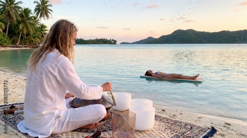 Sound healer playing handpan for client in tropical lagoon