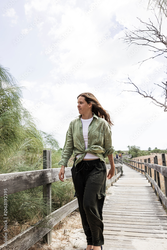 Fototapeta premium Young woman walking along beach boardwalk capturing authentic fashion and everyday coastal style
