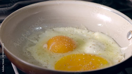 Frying and seasoning eggs in a pan. Yellow yolks glisten over a lightly cooked white.
