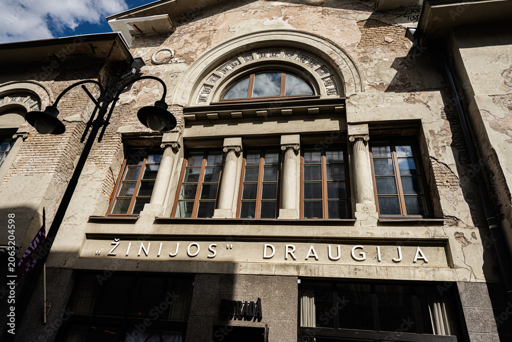 Naklejka premium Historic weathered facade of Žinijos Draugija building in Vilnius, Lithuania with classical columns and arched windows