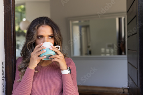 African American woman standing in doorway sipping two-toned ceramic mug, showing white smartwatch