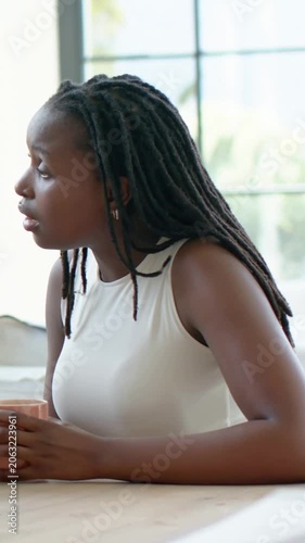 Vertical video: Hearing offscreen voice, she in white top moving mug, gesturing at table by window