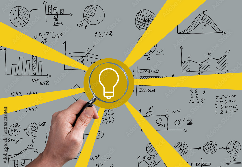 Fototapeta premium Magnifying glass highlights a light bulb among business charts for data insight.