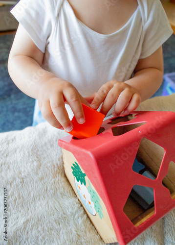Billede på lærred A little boy is putting shapes into a wooden sorter shaped like a house