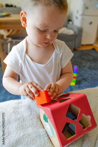 Fotografi A little boy is putting shapes into a wooden sorter shaped like a house