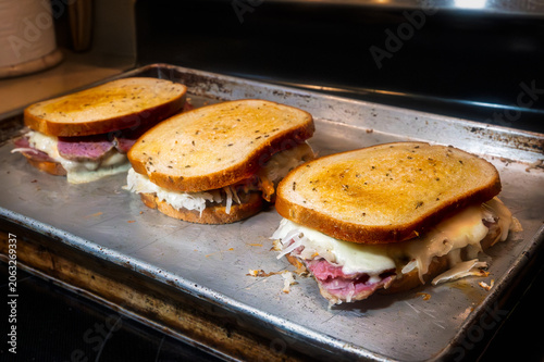 Three Reuben sandwiches on seeded rye bread, toasted in the oven on a sheet pan