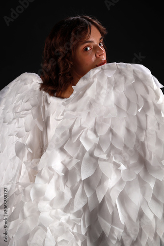 Medium shot of a beautiful woman in a golden corset and white angel wings standing with her back turned and looking over her shoulder