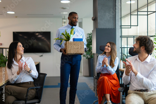Employee leaving job with items in a box while colleagues clapping
