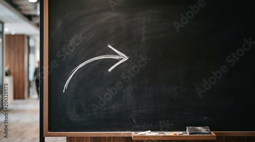 A chalkboard with a simple white arrow drawn in chalk. The background is dark and smooth, suggesting a classroom or meeting space.