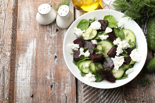 Quadro su tela Tasty salad with boiled beet, cucumbers, feta cheese and dill on wooden table, flat lay