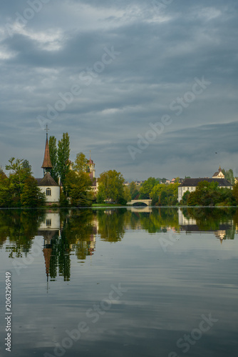 Reflection of buildings and trees on calm water under a cloudy sky in a small town
