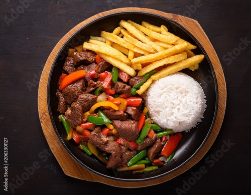 delicious peruvian beef lomo saltado with stir fried vegetables fries and rice in black pan overhead shot