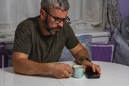 Man enjoying coffee and using smartphone at home office during work break