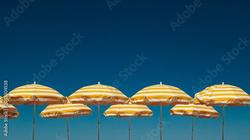 Bright yellow and white striped beach umbrellas stand against a clear deep blue sky on a sunny summer vacation day