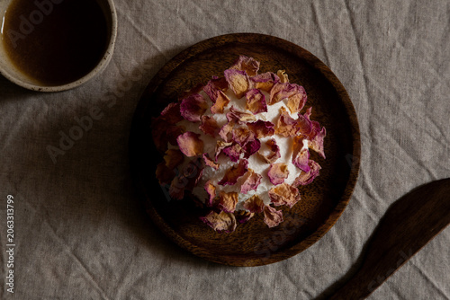 Goat cheese sphere decorated with dried rose petals served on a wooden plate on linen tablecloth.