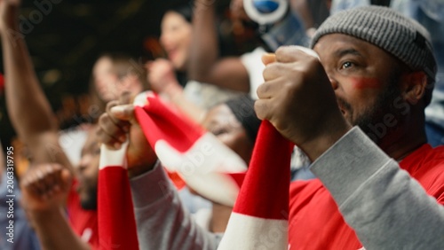 Fotografía Organized fan club waving scarves celebrating in the terrace stands, thrilling football match in a crowded stadium, active fans create synchronized fan chants