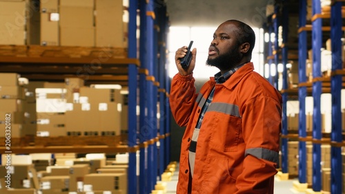 Bild auf Leinwand African american worker transmitting information via walkie-talkie radio signal, internal depot communication to ensure express delivery and quality operations, distribution hub