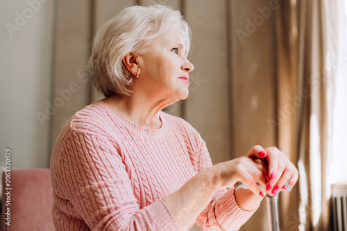 Obraz na plátně Elderly beautiful woman contemplating, holding cane, looking out window